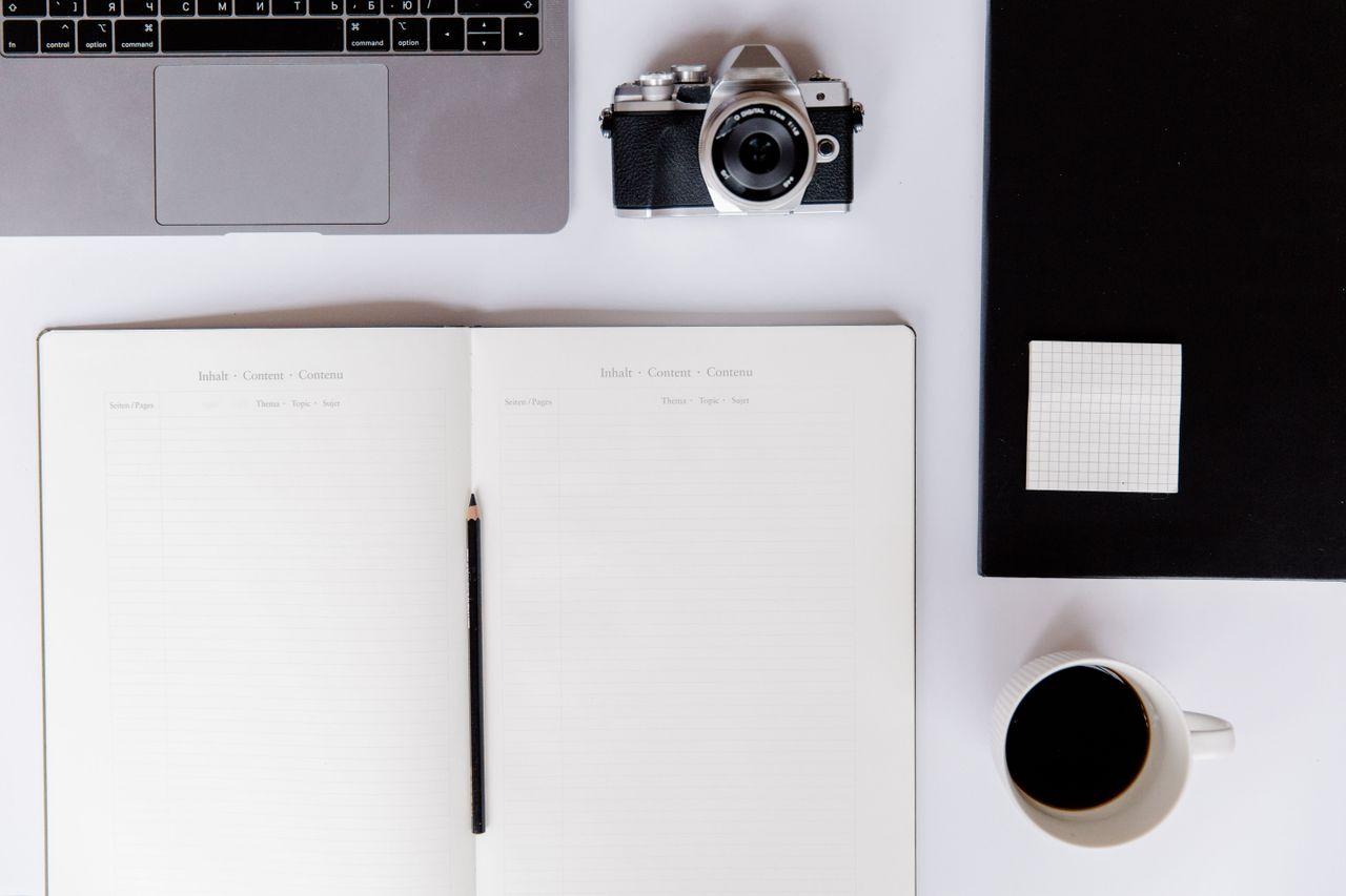Laptop, open notebook, camera and coffee on a desk